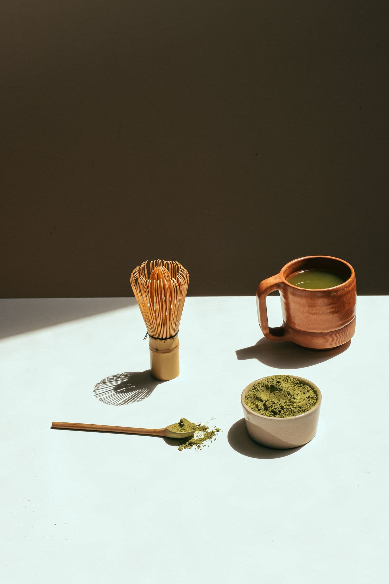 Fouet en bambou, tasse de matcha et poudre de thé vert sous une lumière chaude